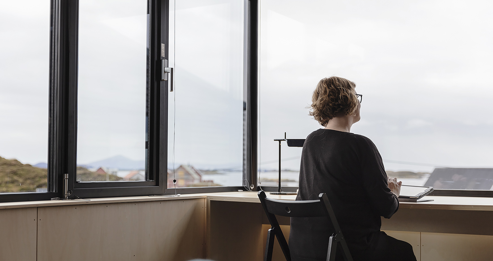 woman at desk in front of large windows looking out over coastline view